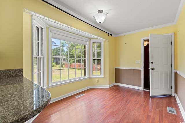 unfurnished dining area featuring wood finished floors, ornamental molding, and baseboards
