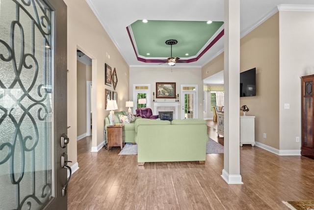foyer featuring a ceiling fan, baseboards, wood finished floors, crown molding, and a raised ceiling