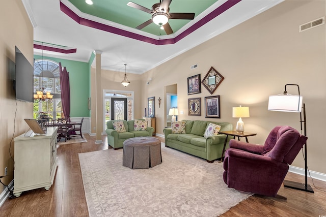 living area with a tray ceiling, crown molding, wood finished floors, a chandelier, and a ceiling fan