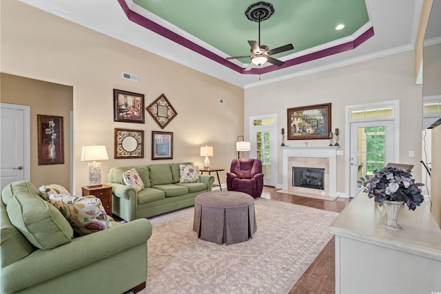living room featuring ceiling fan, a raised ceiling, ornamental molding, wood finished floors, and a fireplace with flush hearth
