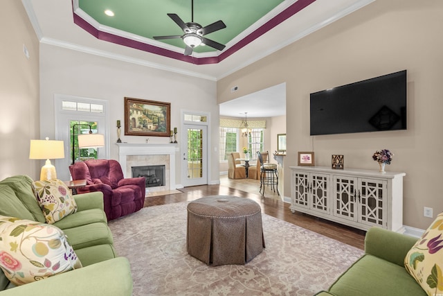 living area with crown molding, wood finished floors, a ceiling fan, a raised ceiling, and a high end fireplace