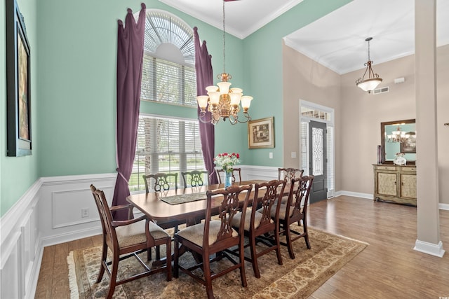 dining area featuring a chandelier, a high ceiling, ornamental molding, wood finished floors, and a wainscoted wall