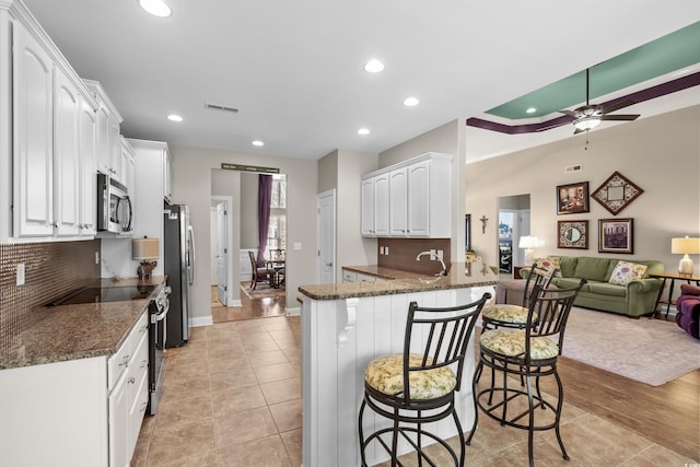 kitchen with appliances with stainless steel finishes, a breakfast bar area, white cabinetry, dark stone counters, and ceiling fan