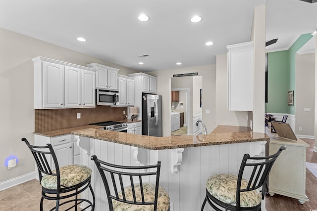 kitchen featuring stainless steel appliances, a peninsula, stone countertops, tasteful backsplash, and white cabinets