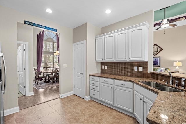 kitchen featuring a sink, ceiling fan, stone counters, white cabinetry, and baseboards