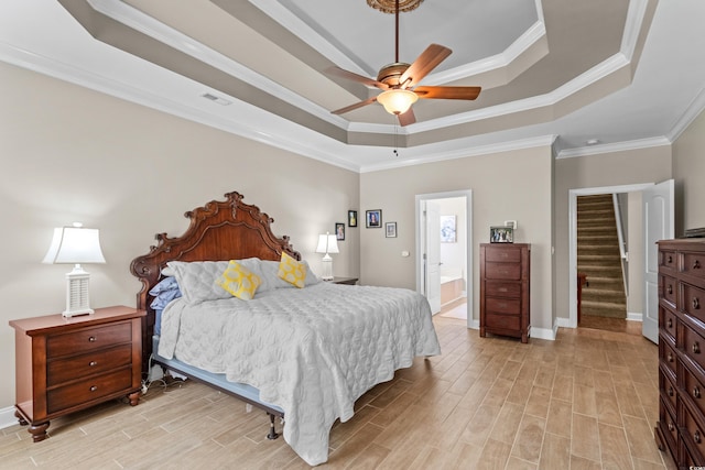 bedroom with a tray ceiling, light wood finished floors, crown molding, and baseboards