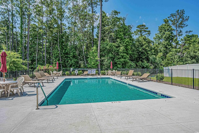community pool featuring a patio, fence, and view of scattered trees
