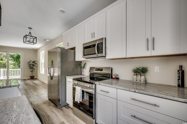 1673 Carriage Ln, Little River, SC 29566 - kitchen with appliances with stainless steel finishes, light wood-style flooring, white cabinetry, light stone counters, and decorative light fixtures