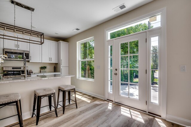 1673 Carriage Ln, Little River, SC 29566 - kitchen featuring appliances with stainless steel finishes, a breakfast bar, light wood-style flooring, and light stone countertops