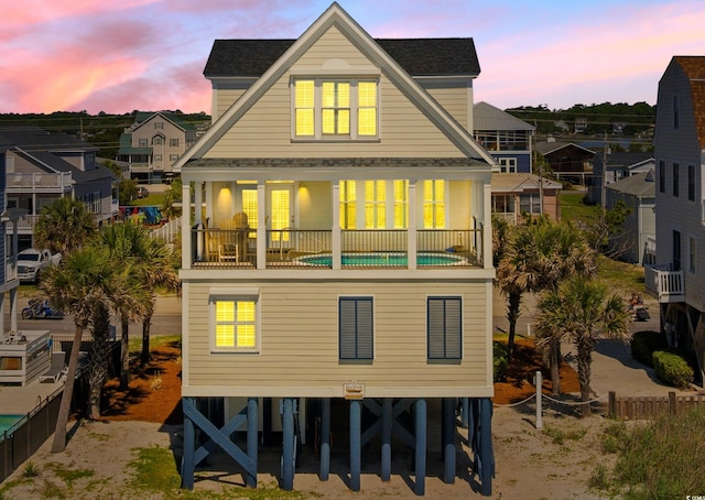 703 S Waccamaw Dr, Garden City Beach, SC 29576 - back of house at dusk with a shingled roof, a balcony, and fence