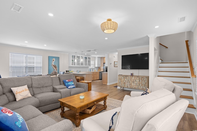 living room featuring light wood finished floors, crown molding, recessed lighting, stairs, and baseboards