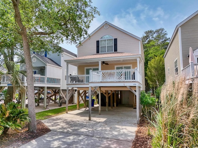 beach home featuring concrete driveway, a carport, ceiling fan, covered porch, and stairway