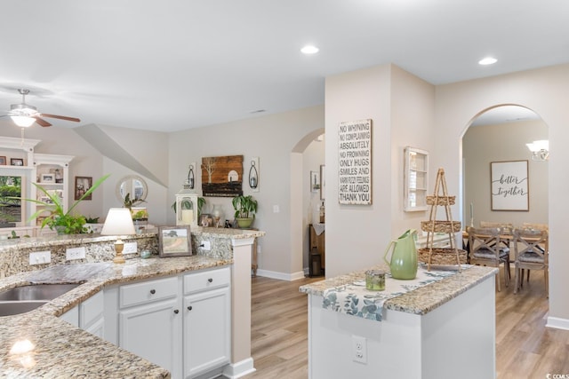kitchen with arched walkways, a ceiling fan, light wood finished floors, white cabinets, and light stone countertops