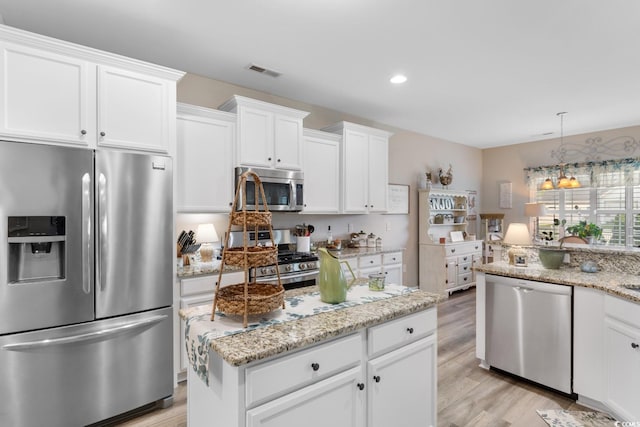 kitchen with appliances with stainless steel finishes, light wood-style floors, white cabinetry, light stone counters, and hanging light fixtures