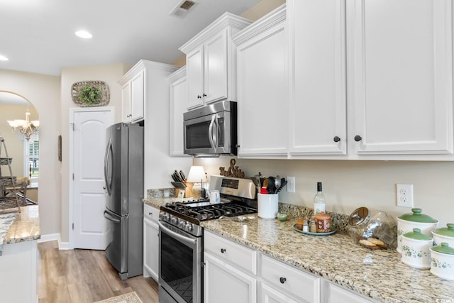 kitchen with appliances with stainless steel finishes, white cabinets, light wood-style flooring, a chandelier, and light stone counters