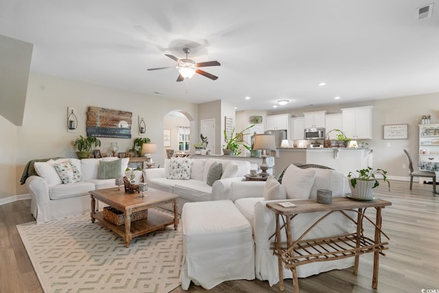 living room with arched walkways, ceiling fan, light wood-style flooring, baseboards, and recessed lighting