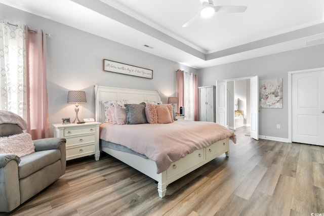 bedroom featuring wood finished floors, a raised ceiling, crown molding, ensuite bathroom, and baseboards