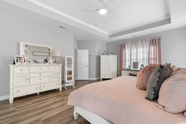 bedroom with a tray ceiling, dark wood-style flooring, ornamental molding, baseboards, and ceiling fan