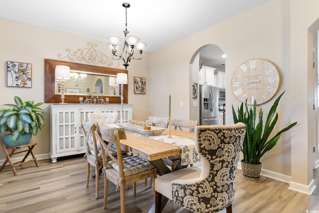 dining area featuring a chandelier, arched walkways, light wood finished floors, and baseboards