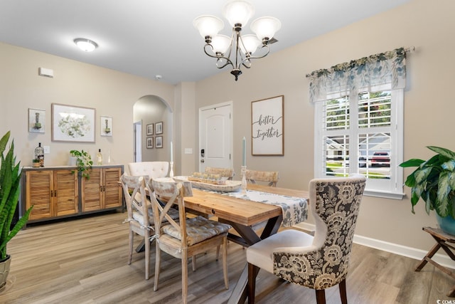 dining room featuring arched walkways, light wood finished floors, a chandelier, and baseboards