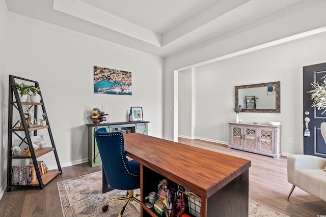 home office with a raised ceiling, wood finished floors, and baseboards