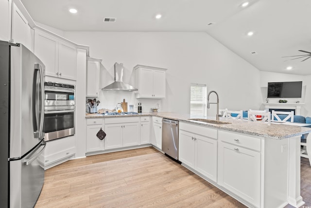 kitchen with appliances with stainless steel finishes, a sink, a peninsula, lofted ceiling, and wall chimney range hood