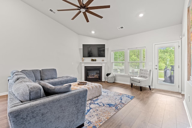 living area with ceiling fan, vaulted ceiling, wood finished floors, a glass covered fireplace, and recessed lighting