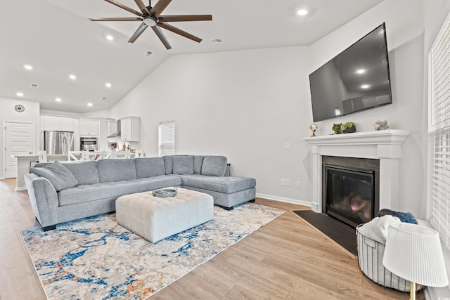 living area featuring a ceiling fan, a fireplace with flush hearth, recessed lighting, light wood-style flooring, and high vaulted ceiling
