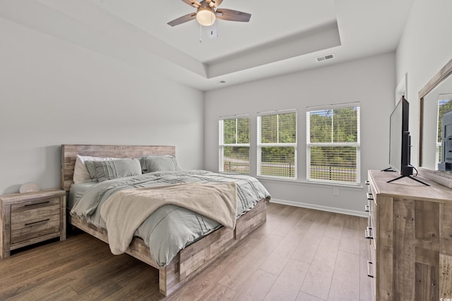 bedroom featuring wood finished floors, a tray ceiling, and baseboards