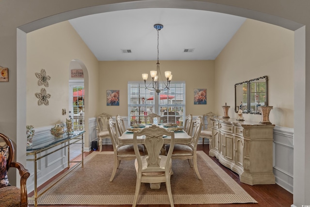 dining area with arched walkways, a chandelier, dark wood-style floors, and wainscoting