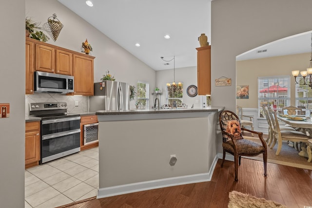 kitchen featuring appliances with stainless steel finishes, a chandelier, high vaulted ceiling, brown cabinets, and healthy amount of natural light