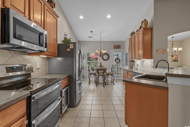 kitchen with stainless steel appliances, a chandelier, a sink, dark countertops, and brown cabinetry