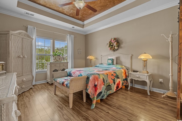 bedroom with a tray ceiling, wood finished floors, crown molding, baseboards, and a ceiling fan