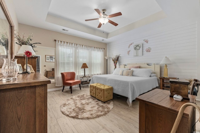 605 Ginger Lily Way, Little River, SC 29566 - bedroom featuring a tray ceiling, light wood-style flooring, ceiling fan, and wooden walls