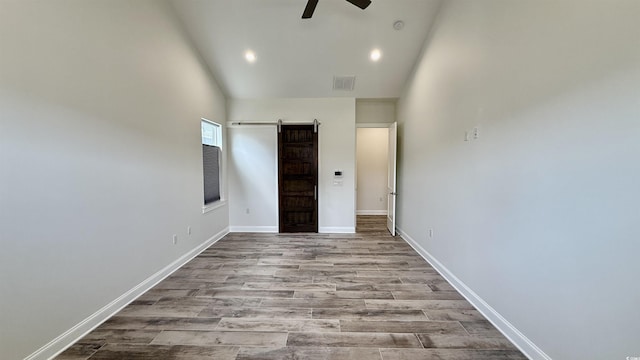 unfurnished bedroom featuring a barn door, high vaulted ceiling, baseboards, wood finished floors, and recessed lighting