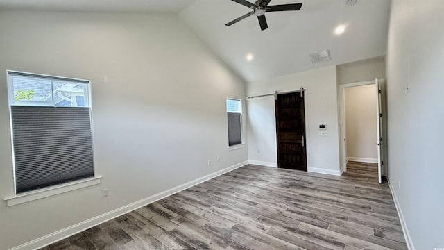 unfurnished bedroom with high vaulted ceiling, a barn door, multiple windows, wood finished floors, and baseboards