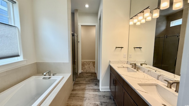 full bathroom featuring wood finished floors, a bath, double vanity, an enclosed shower, and baseboards