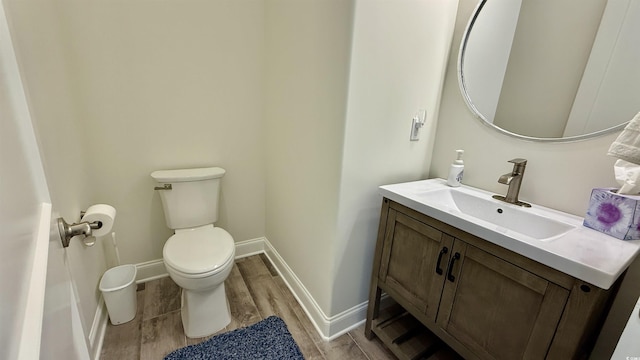 half bathroom with wood finished floors, toilet, vanity, and baseboards