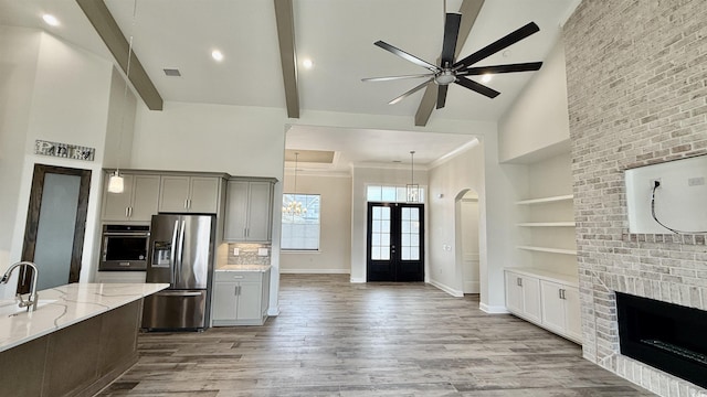 kitchen featuring stainless steel appliances, high vaulted ceiling, a ceiling fan, light stone counters, and wood finished floors