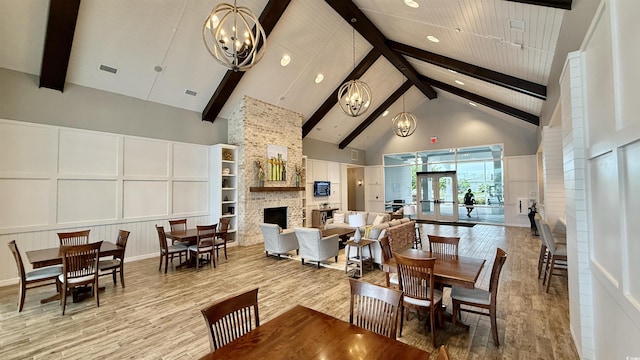 dining area featuring a stone fireplace, high vaulted ceiling, beamed ceiling, a chandelier, and wood finished floors