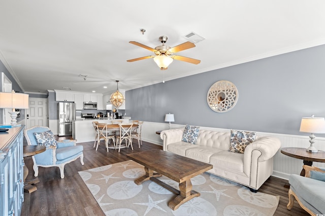 living room with dark wood-style floors, ornamental molding, ceiling fan, and wainscoting