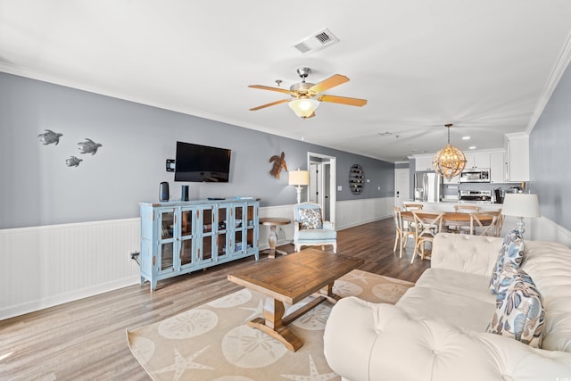 living area featuring wood finished floors, ornamental molding, wainscoting, a ceiling fan, and a chandelier