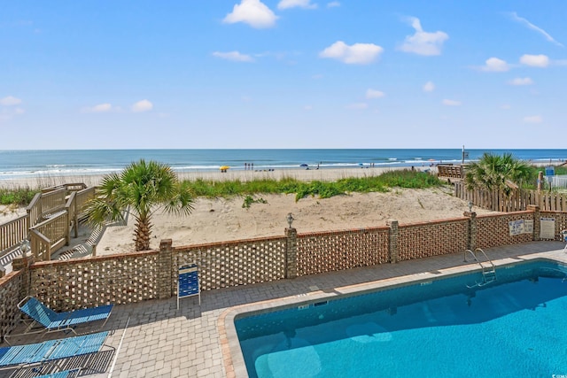community pool featuring view of water and beach, a patio, and fence