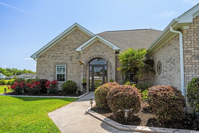 doorway to property with brick siding, a yard, and a shingled roof