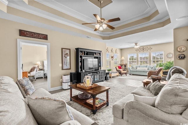 living area featuring a raised ceiling, ornamental molding, ceiling fan, and baseboards