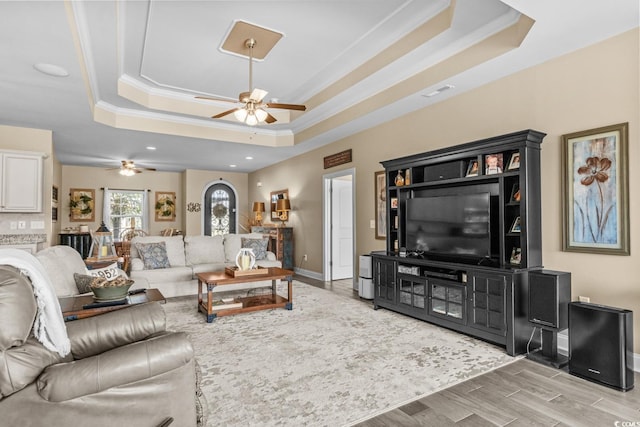 living room featuring a tray ceiling, ceiling fan, ornamental molding, baseboards, and wood finished floors
