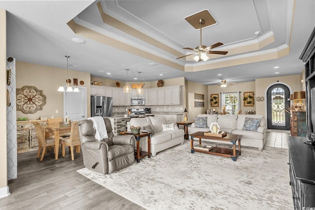 living area featuring a raised ceiling, ornamental molding, ceiling fan, recessed lighting, and light wood-type flooring