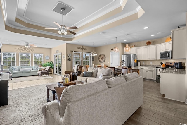 living room with ornamental molding, a tray ceiling, a ceiling fan, dark wood-style floors, and recessed lighting