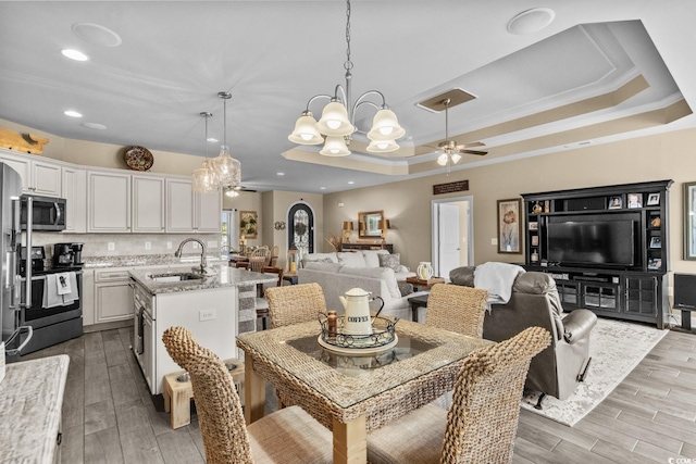 dining space featuring a ceiling fan, a chandelier, a tray ceiling, wood finished floors, and recessed lighting
