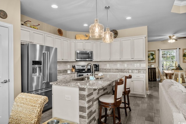 kitchen featuring appliances with stainless steel finishes, a sink, white cabinets, an island with sink, and light stone counters